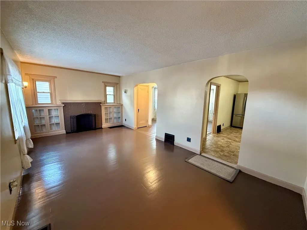 Unfurnished living room featuring a brick fireplace and a textured ceiling