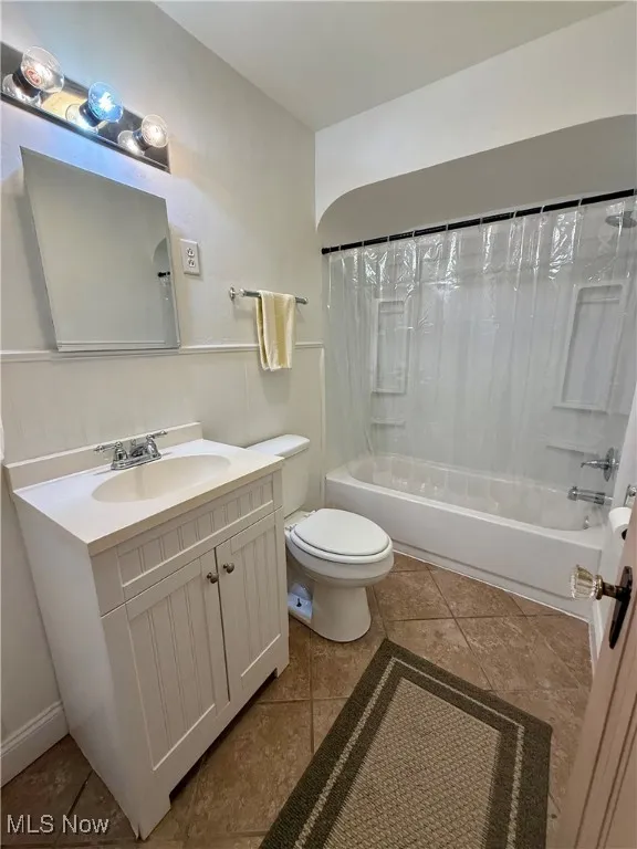 Full bathroom featuring tile patterned flooring, toilet, vanity, and shower / tub combo with curtain
