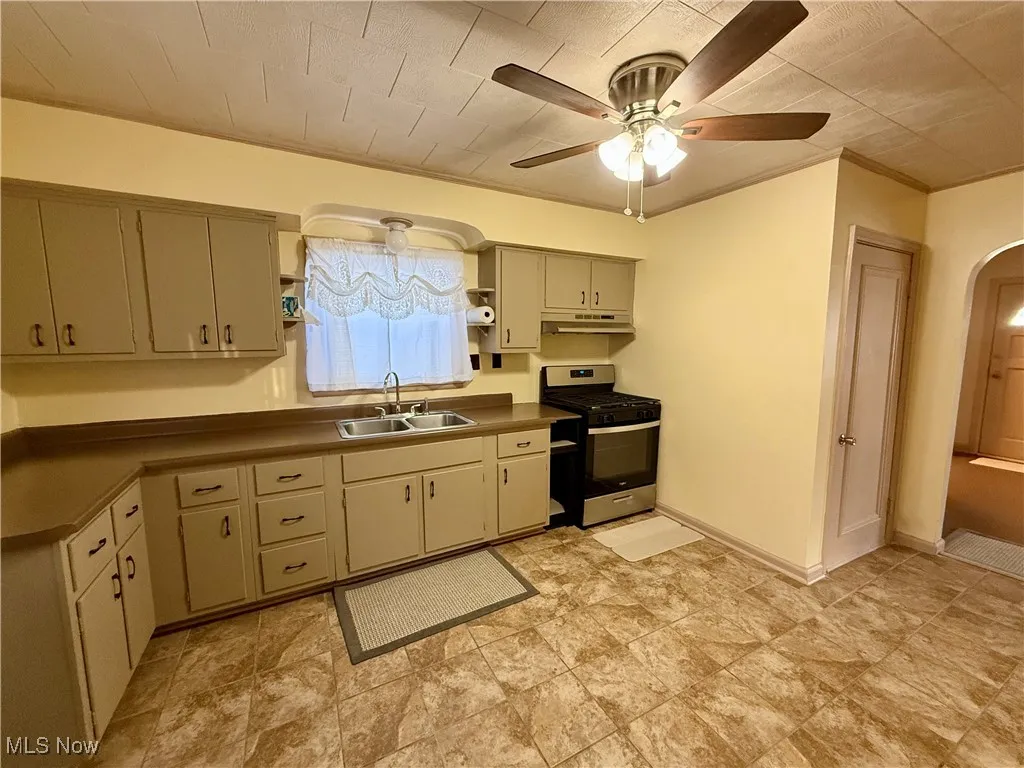 Kitchen with ceiling fan, ornamental molding, stainless steel range with gas stovetop, and sink