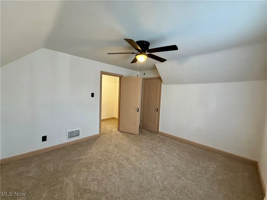 Additional living space with ceiling fan, light colored carpet, and lofted ceiling
