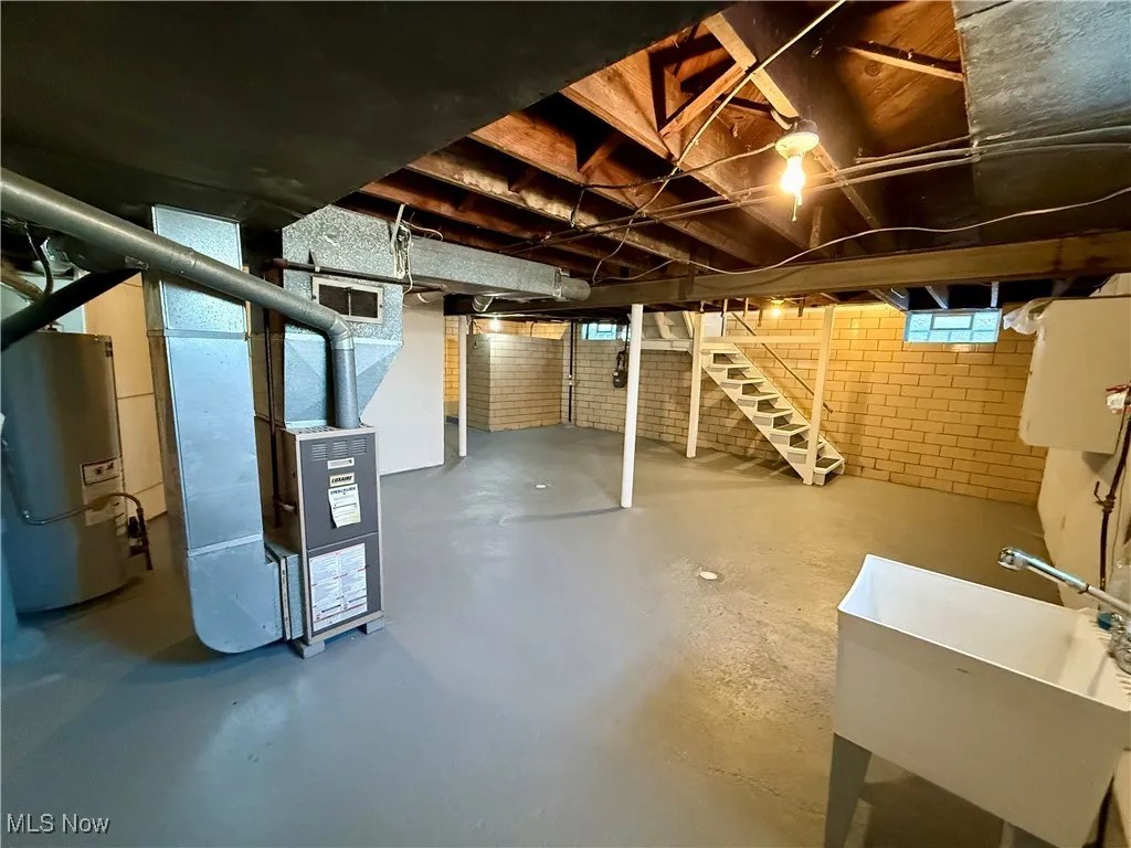 Basement with heating unit, sink, brick wall, and gas water heater