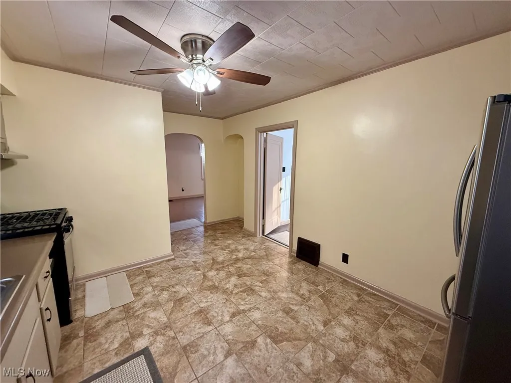 Kitchen featuring ceiling fan, stainless steel refrigerator, white cabinetry, and ornamental molding