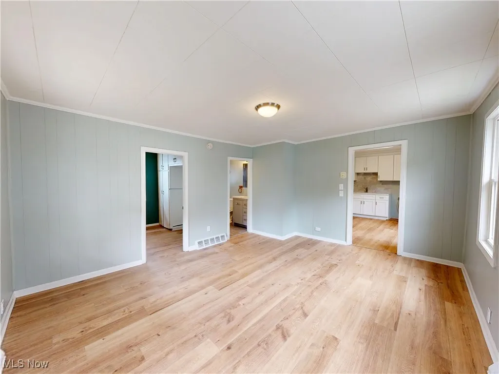 Empty room with light wood-style floors, ornamental molding, and baseboards