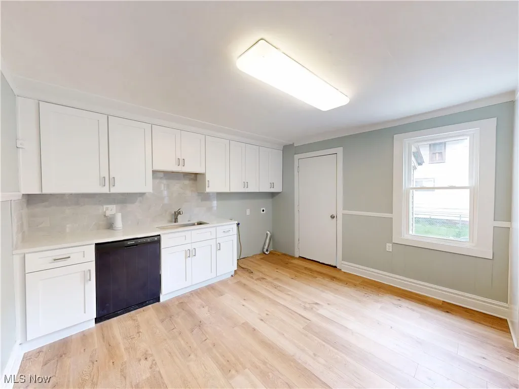 Kitchen with black dishwasher, a sink, light wood-type flooring, and white cabinets