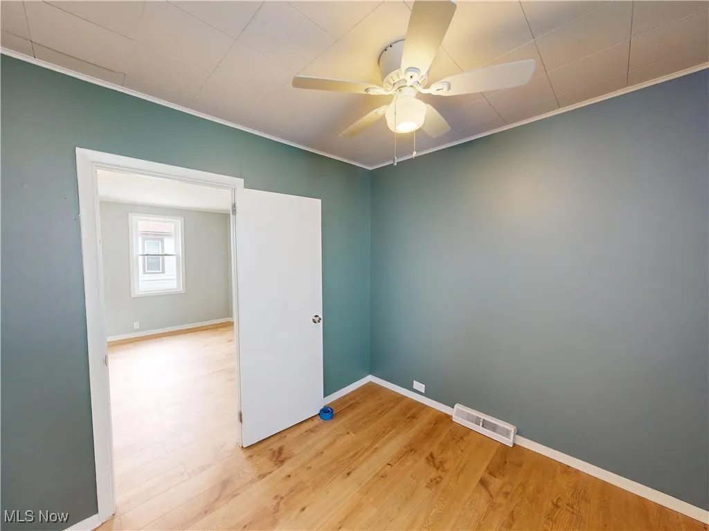 Unfurnished room with ceiling fan, wood finished floors, ornamental molding, and baseboards