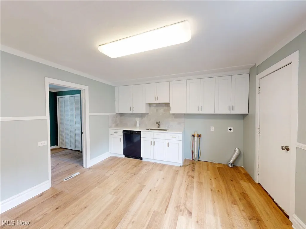 Kitchen featuring black dishwasher, a sink, white cabinets, light wood finished floors, and crown molding
