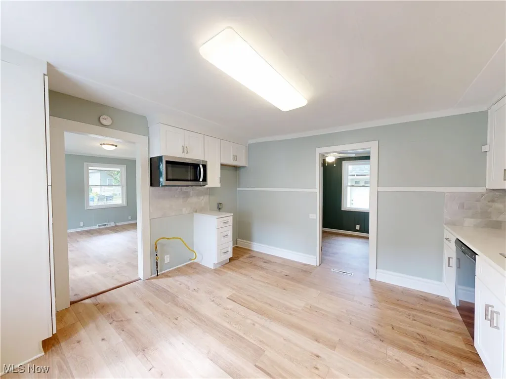 Kitchen featuring stainless steel microwave, dishwashing machine, white cabinets, and healthy amount of natural light