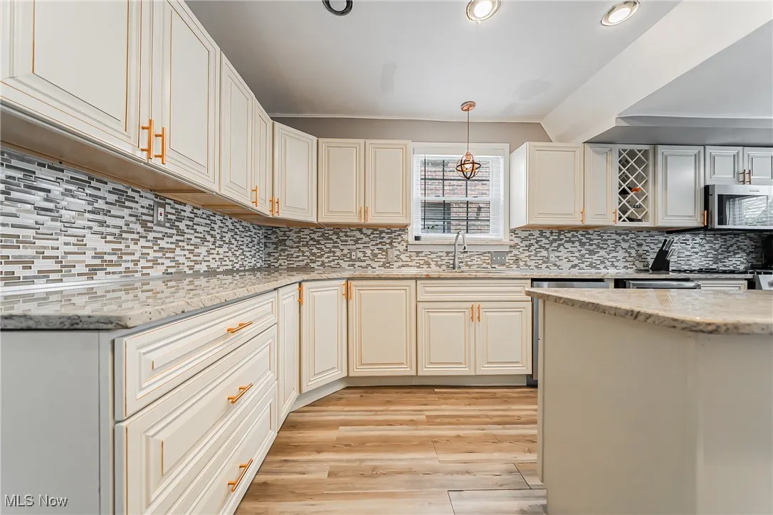 Kitchen with stainless steel microwave, light wood-type flooring, backsplash, light stone countertops, and hanging light fixtures