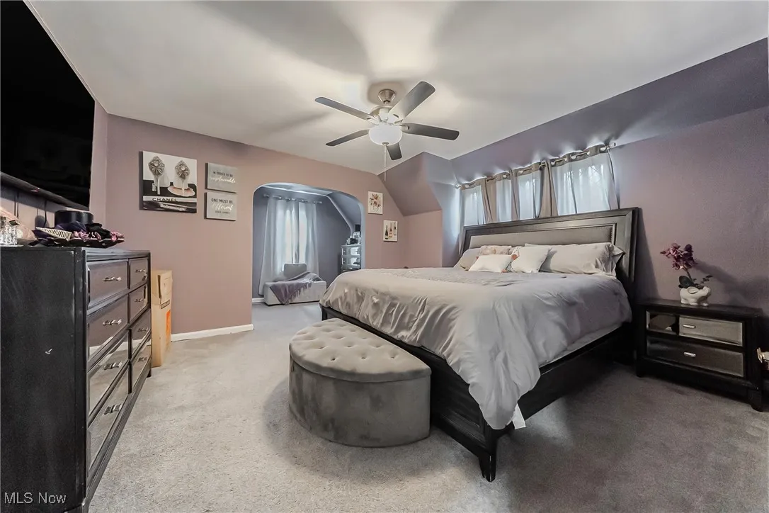 Bedroom featuring light carpet, ceiling fan, and arched walkways