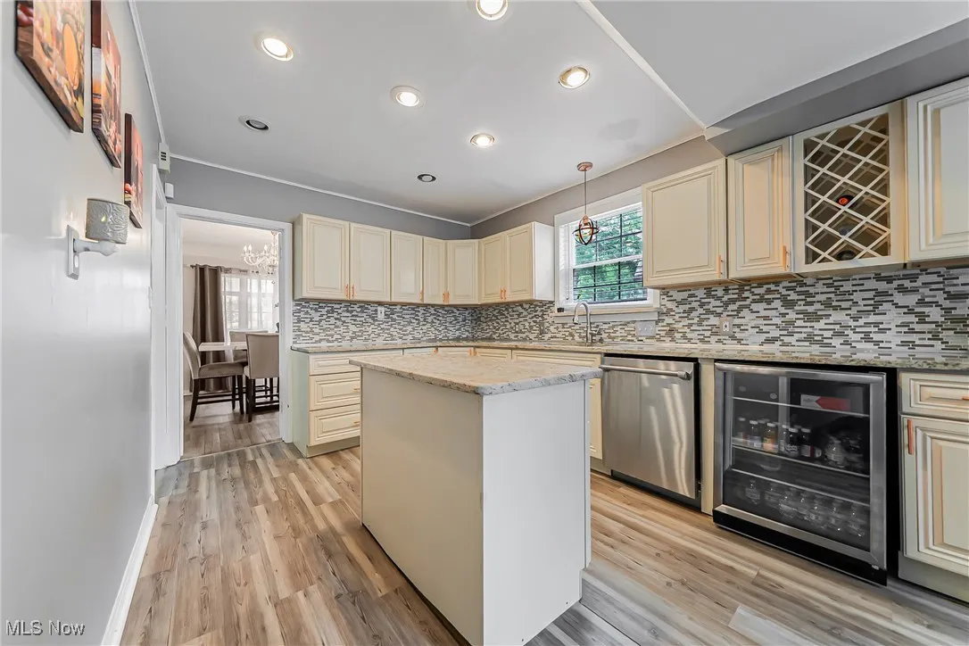Kitchen featuring dishwasher, beverage cooler, cream cabinetry, decorative backsplash, and a center island