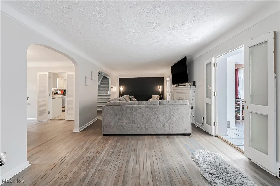 Living area with a textured ceiling, light wood finished floors, arched walkways, and stairs