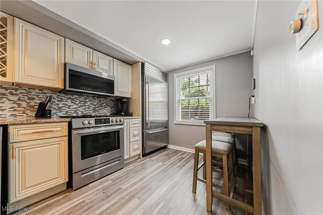 Kitchen with appliances with stainless steel finishes, cream cabinets, tasteful backsplash, light wood-style flooring, and recessed lighting