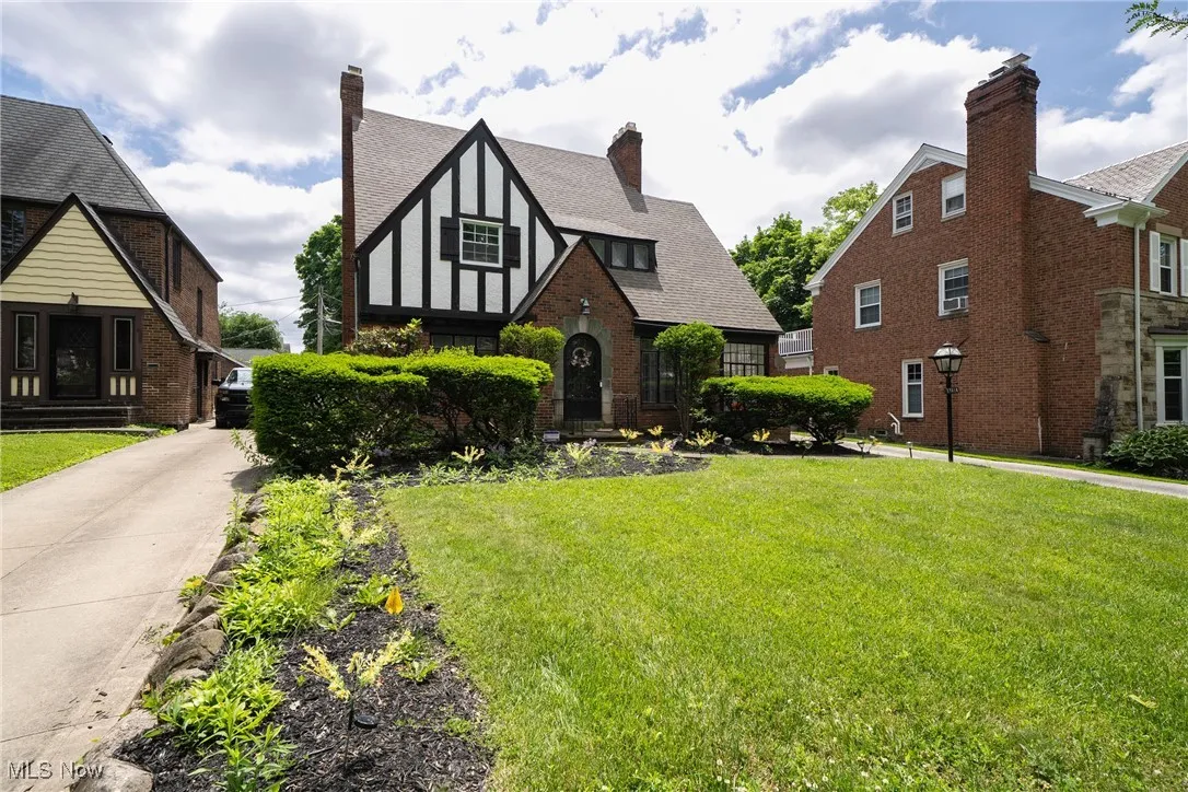 English style home featuring a front lawn, a chimney, roof with shingles, and brick siding