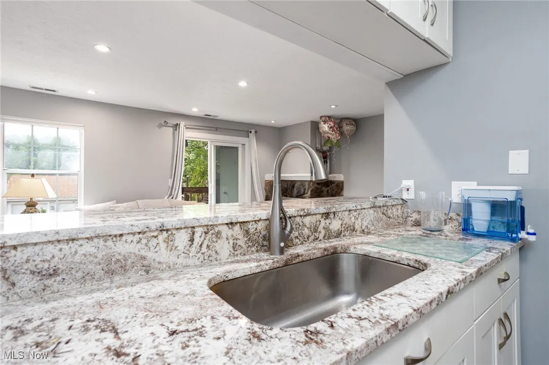 Kitchen featuring a sink, recessed lighting, light stone counters, and white cabinetry
