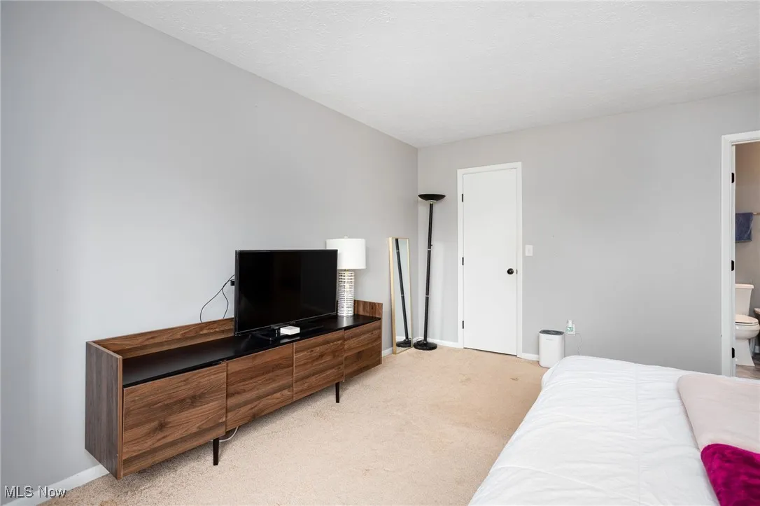 Bedroom featuring light colored carpet, baseboards, and ensuite bath
