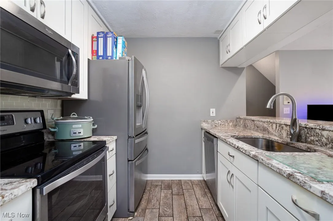 Kitchen featuring stainless steel appliances, a sink, dark wood-style flooring, white cabinetry, and baseboards