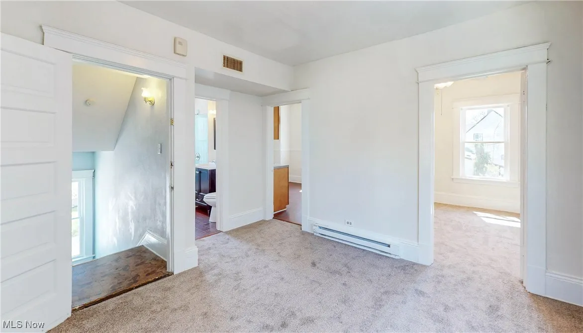 Unfurnished bedroom featuring baseboard heating, carpet flooring, ensuite bath, and baseboards
