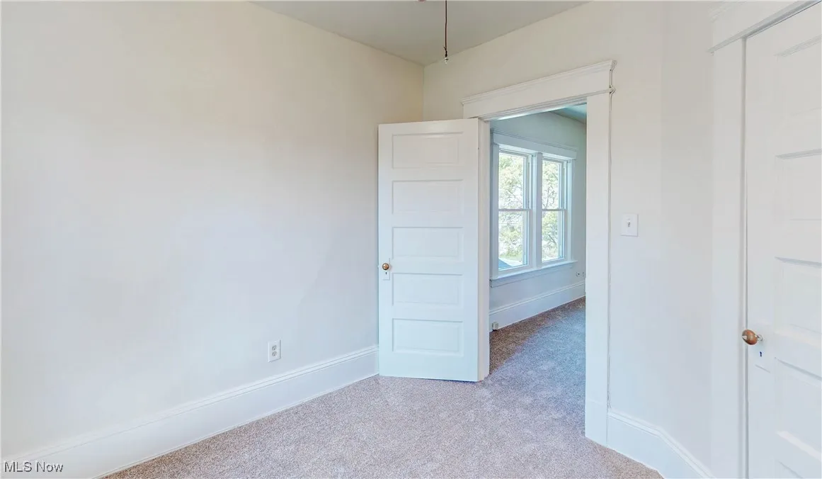 Unfurnished room featuring light carpet and baseboards
