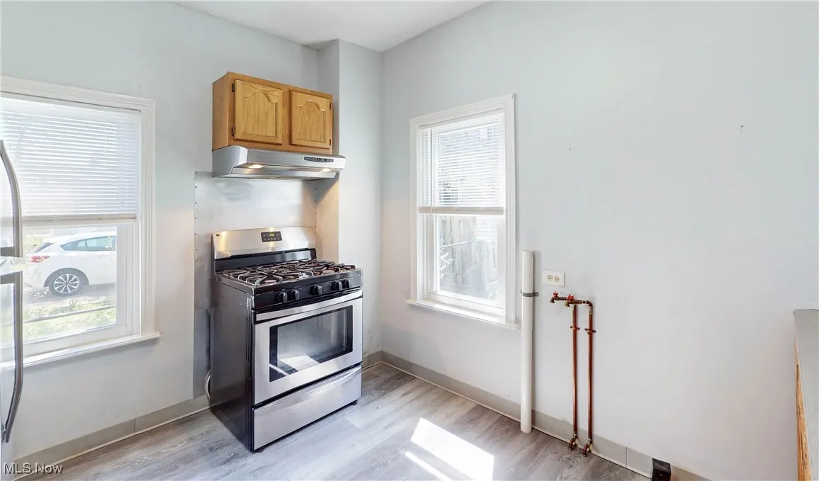 Kitchen featuring stainless steel gas range oven, under cabinet range hood, light wood-style flooring, and baseboards