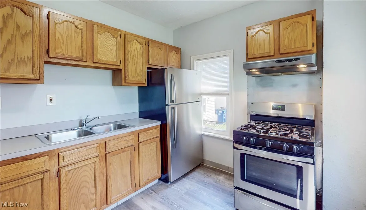 Kitchen with stainless steel appliances, under cabinet range hood, a sink, light wood-style floors, and light countertops