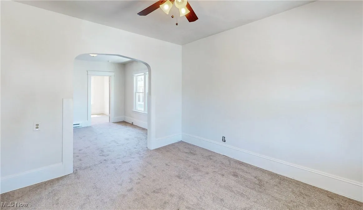 Empty room featuring light colored carpet, arched walkways, ceiling fan, and baseboards