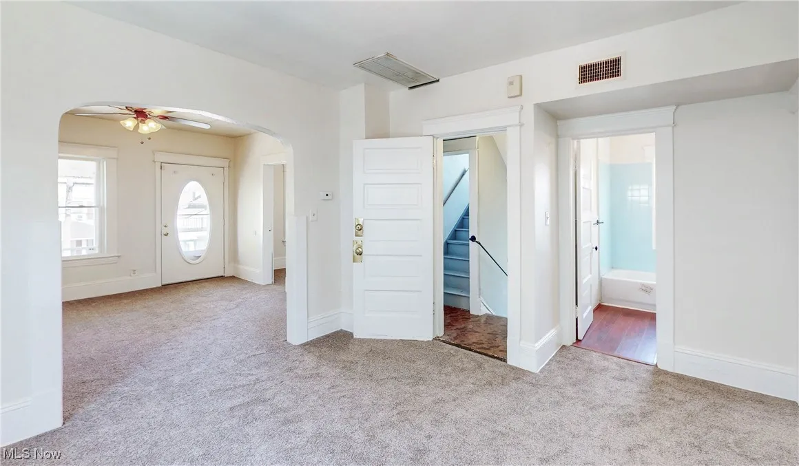 Foyer entrance featuring arched walkways, carpet flooring, a ceiling fan, and stairs