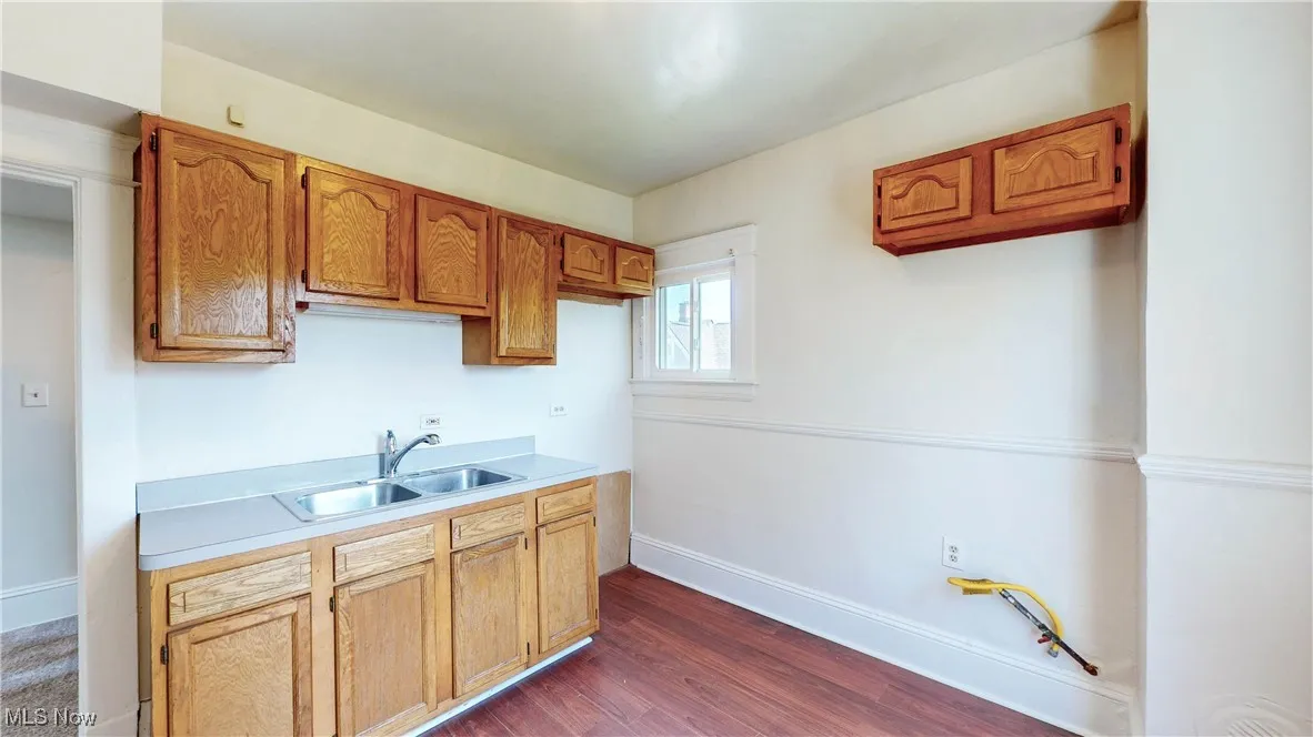 Kitchen featuring a sink, light countertops, dark wood-style floors, baseboards, and brown cabinetry