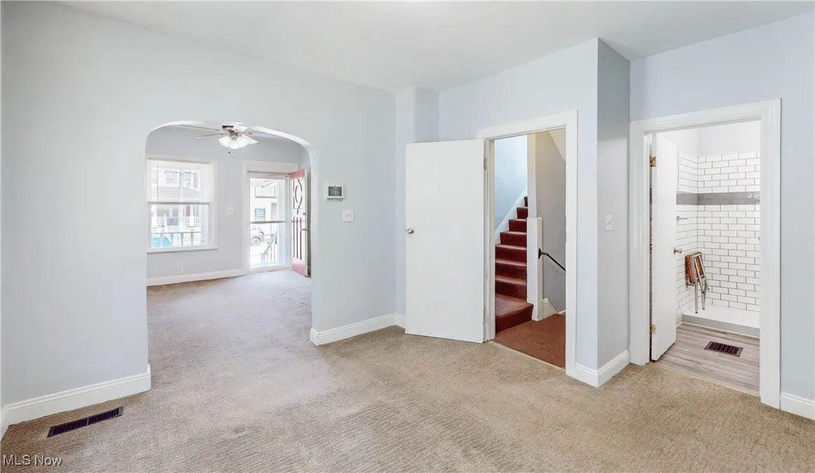Empty room with arched walkways, carpet flooring, stairway, and baseboards