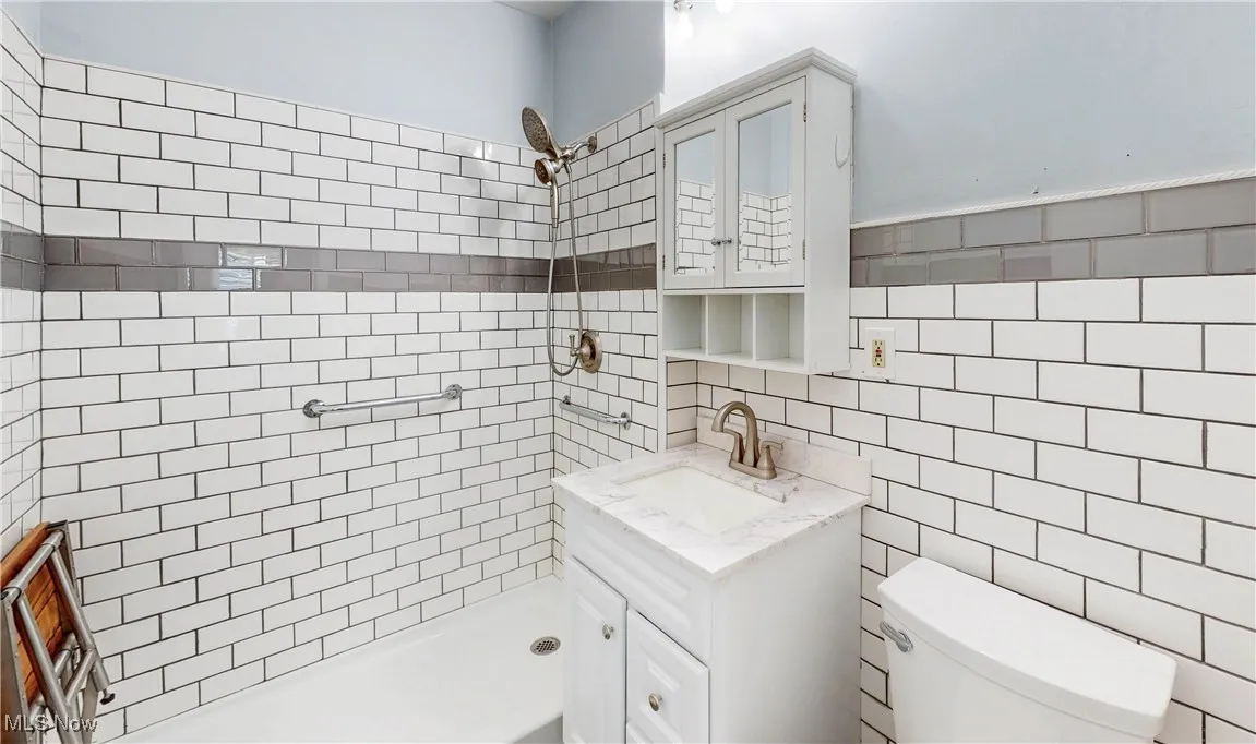 Bathroom with tile walls, a tile shower, toilet, vanity, and tasteful backsplash