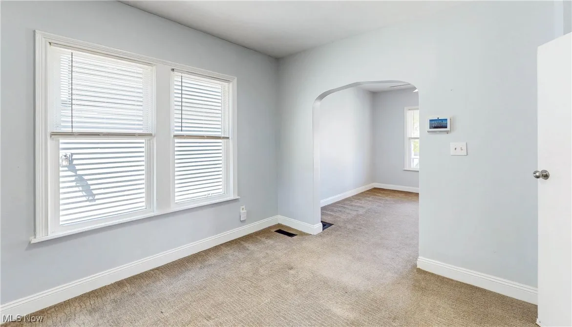 Empty room featuring arched walkways, light colored carpet, and baseboards