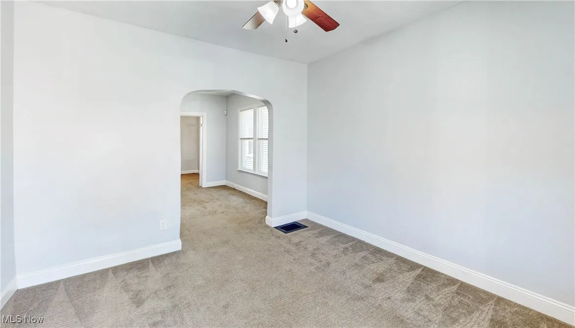 Carpeted empty room with arched walkways, ceiling fan, and baseboards