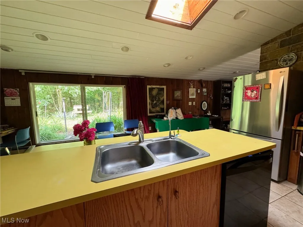 Kitchen featuring freestanding refrigerator, dishwasher, a sink, light tile patterned flooring, and light countertops
