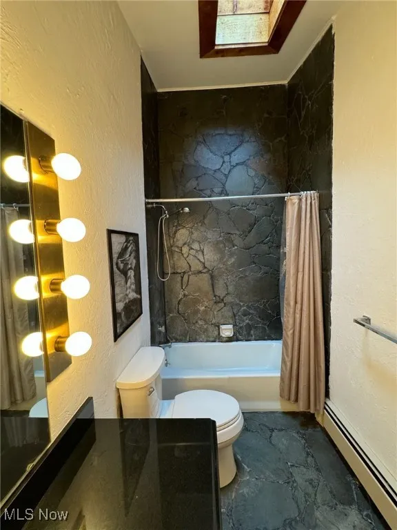 Full bathroom featuring baseboard heating, toilet, shower / bathtub combination with curtain, and a textured wall