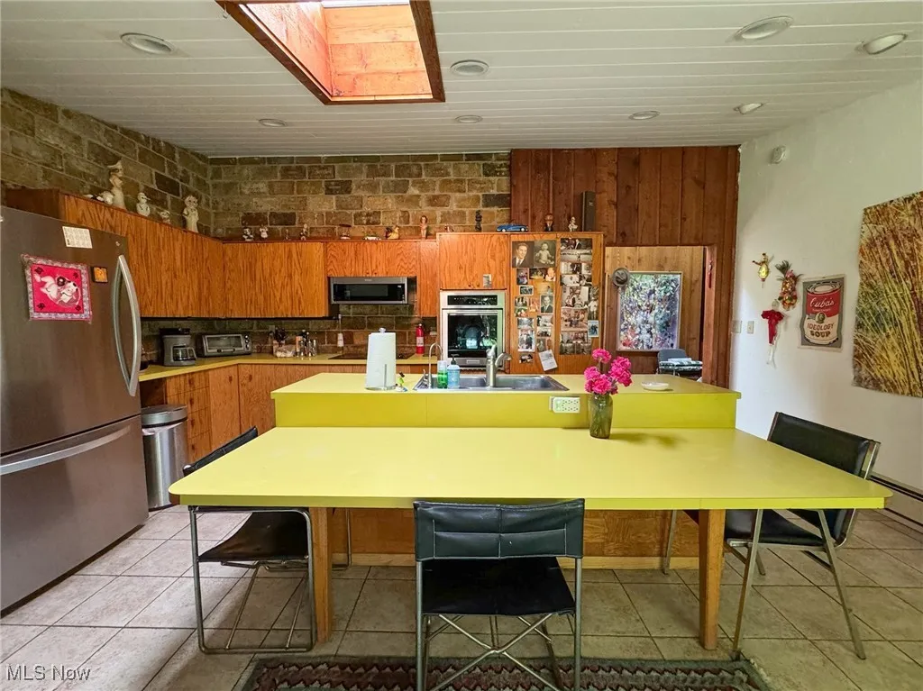 Kitchen with appliances with stainless steel finishes, brown cabinets, recessed lighting, and light tile patterned flooring