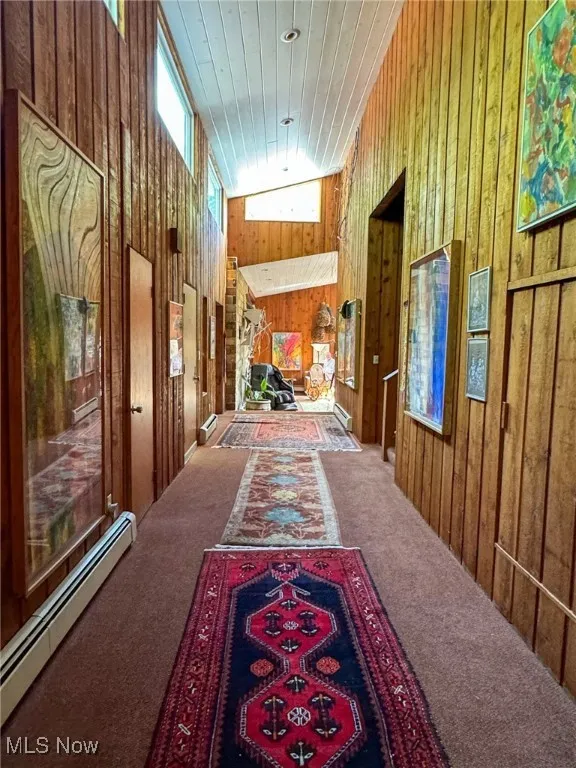 Corridor with carpet floors, a baseboard radiator, wood walls, and wooden ceiling