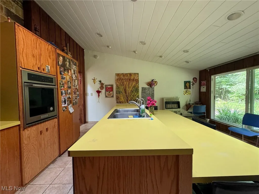 Kitchen featuring a sink, stainless steel oven, light countertops, wood ceiling, and light tile patterned flooring