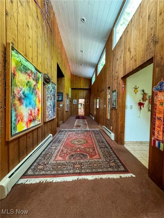 Corridor featuring wood walls, a baseboard radiator, wood ceiling, carpet flooring, and a towering ceiling