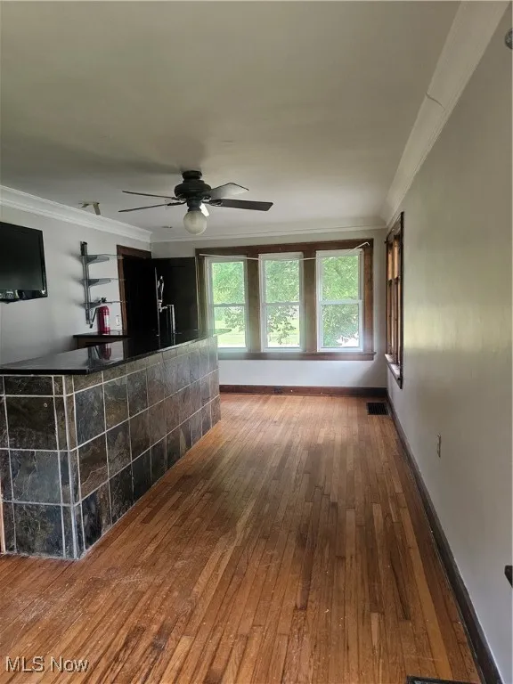 Unfurnished living room with crown molding, hardwood / wood-style floors, a ceiling fan, and bar area