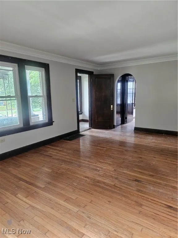 Spare room featuring arched walkways, ornamental molding, plenty of natural light, and light wood-style floors