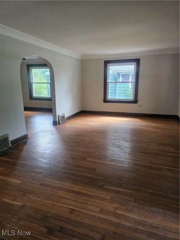 Empty room featuring arched walkways, wood-type flooring, and crown molding