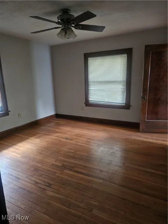 Unfurnished room with plenty of natural light, hardwood / wood-style flooring, a ceiling fan, and a textured ceiling