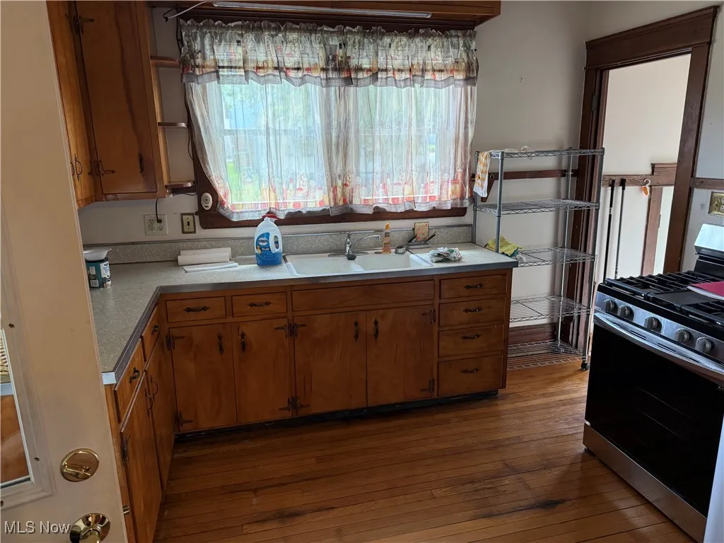 Kitchen with gas range, wood-type flooring, brown cabinetry, and light countertops