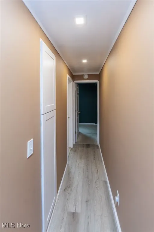 Hallway with light wood-style flooring, crown molding, and baseboards