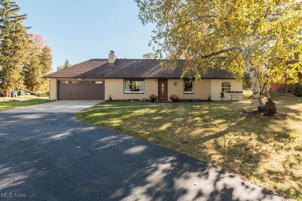 Ranch-style house with asphalt driveway, a chimney, a front lawn, a garage, and a shingled roof