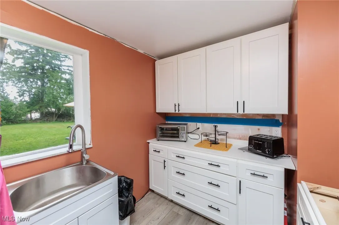 Kitchen featuring a sink, white cabinetry, light countertops, and light wood-style floors