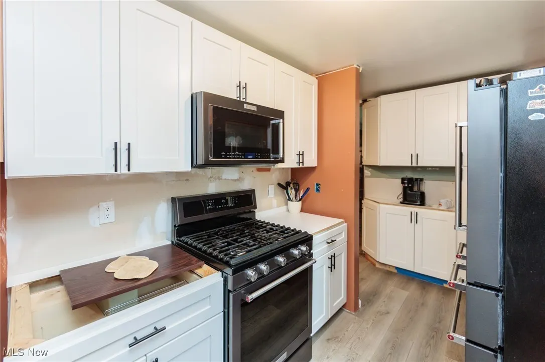 Kitchen featuring gas stove, freestanding refrigerator, white cabinetry, and light wood finished floors