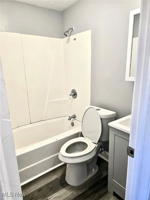 Bathroom featuring vanity, shower / bathtub combination, toilet, wood finished floors, and a textured ceiling