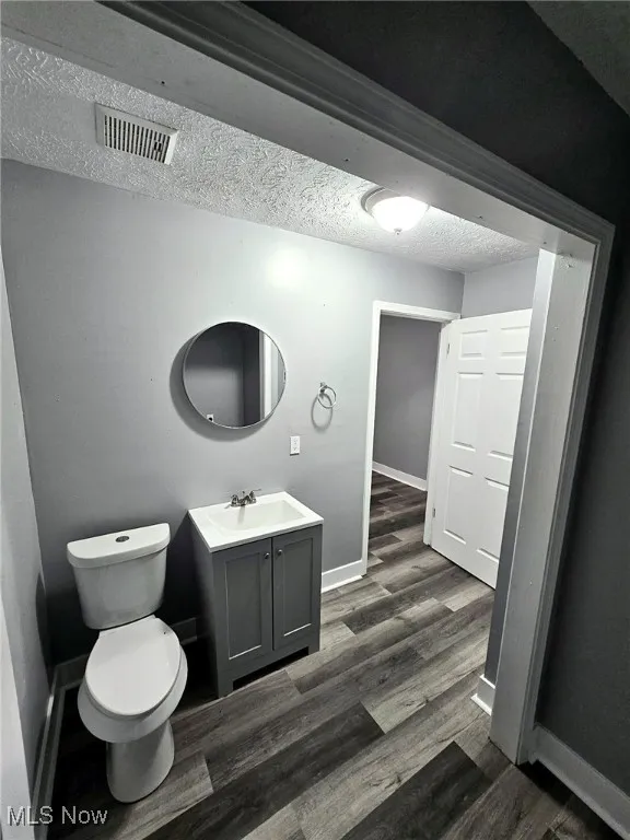 Bathroom featuring vanity, toilet, baseboards, wood finished floors, and a textured ceiling