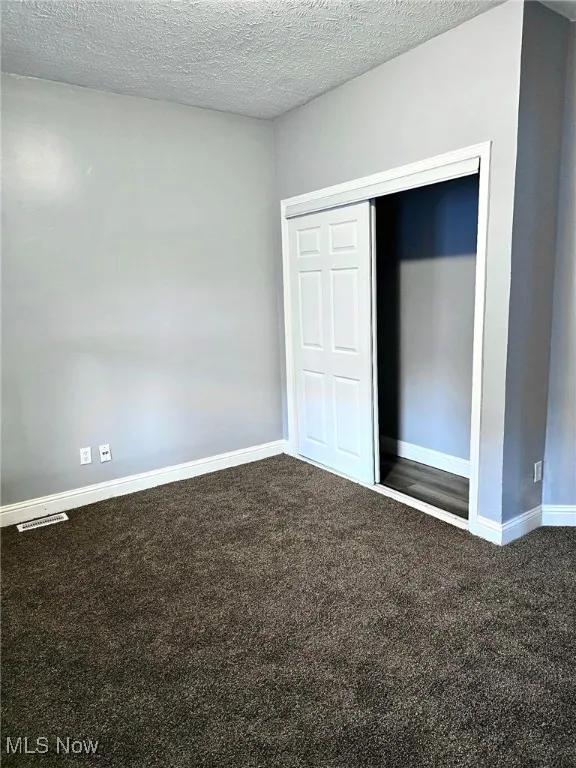 Unfurnished bedroom with carpet flooring, baseboards, a closet, and a textured ceiling