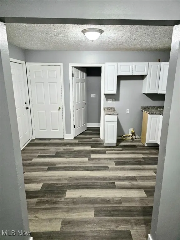 Kitchen with dark wood finished floors, white cabinets, a textured ceiling, and baseboards